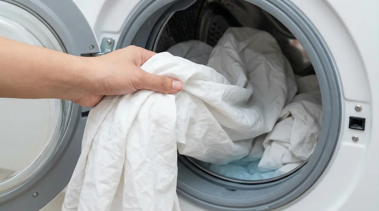 Una mano inserisce lenzuola bianche all'interno di una lavatrice aperta