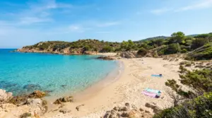 Spiaggia libera con sabbia chiara e mare cristallino circondata da natura mediterranea