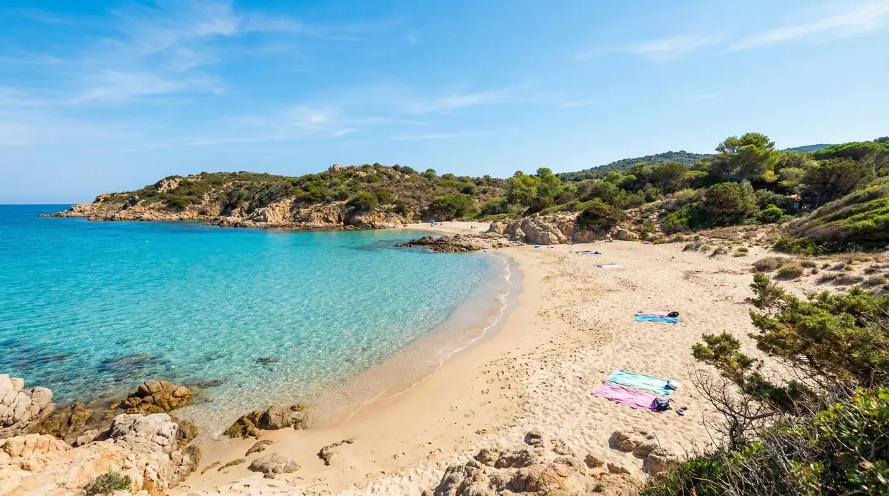 Spiaggia libera con sabbia chiara e mare cristallino circondata da natura mediterranea